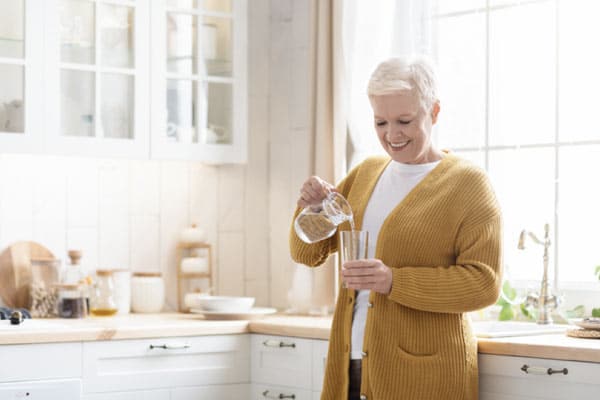 An older woman follows healthy hydration habits for older adults as she pours a glass of water for herself.